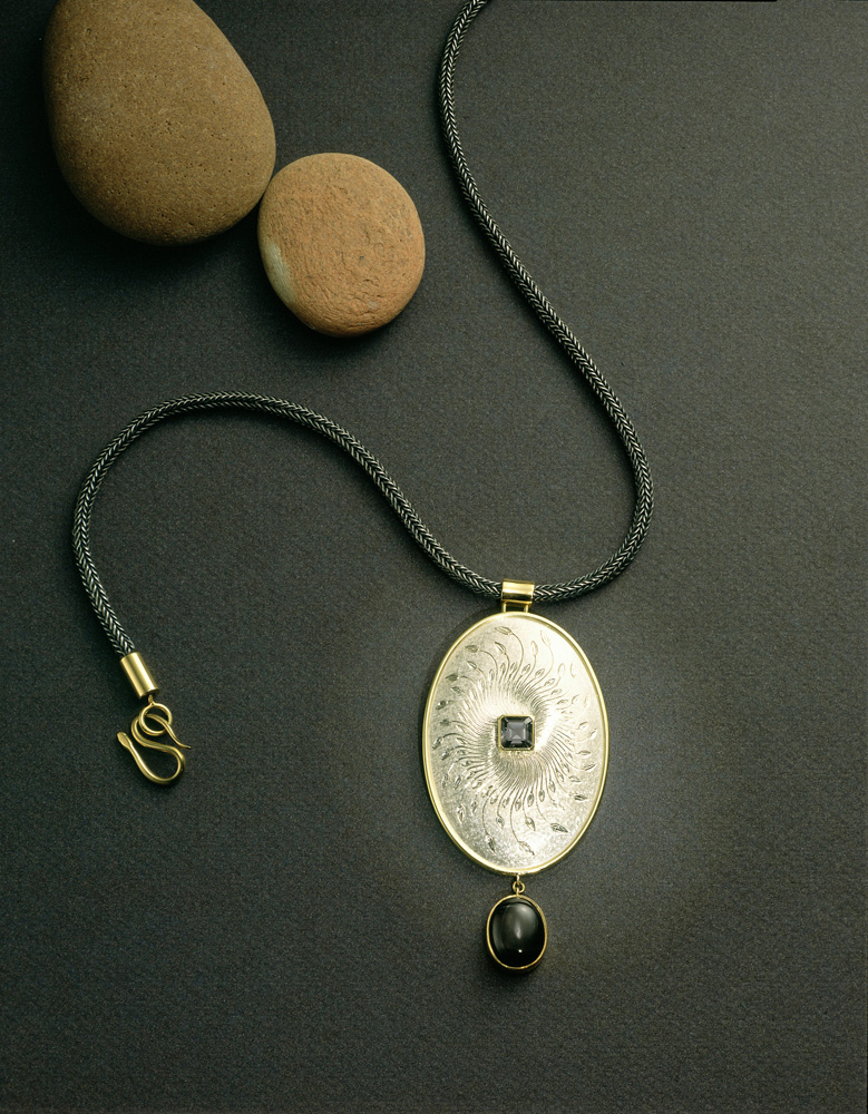 Silver, hand engraved, set with violet/charcoal grey spinel star diopside drop. 83x42mm. Silver hand-knitted sacred knot chain, oxidised with yellow metal clasp and fittings.Photo: Paul Hartley