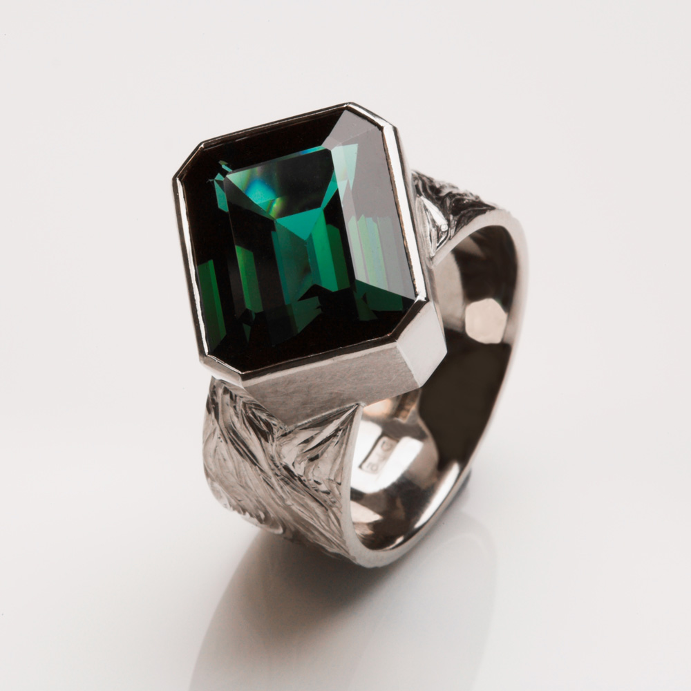 18ct white gold, hand engraved with 'flame of love' design radiating from initial 'K' on the centre back of shank. Stone set diagonally on ring shank. Blue/green tourmaline: 10.1cts.Photo: Simon B Armitt
