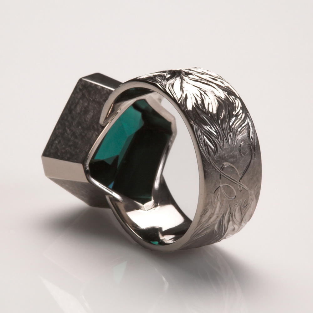 18ct white gold, hand engraved with 'flame of love' design radiating from initial 'K' on the centre back of shank. Stone set diagonally on ring shank. Blue/green tourmaline: 10.1cts. Photo: Simon B Armitt