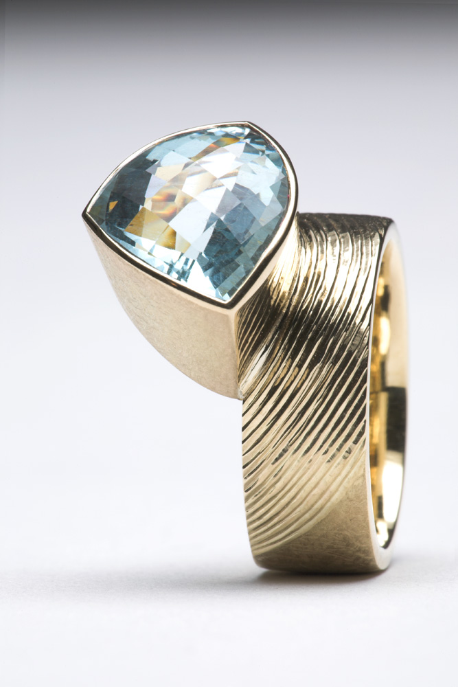 18ct yellow gold, part engraved and part scrubbed. Set with trillion chequerboard cut aquamarine 5.40cts.