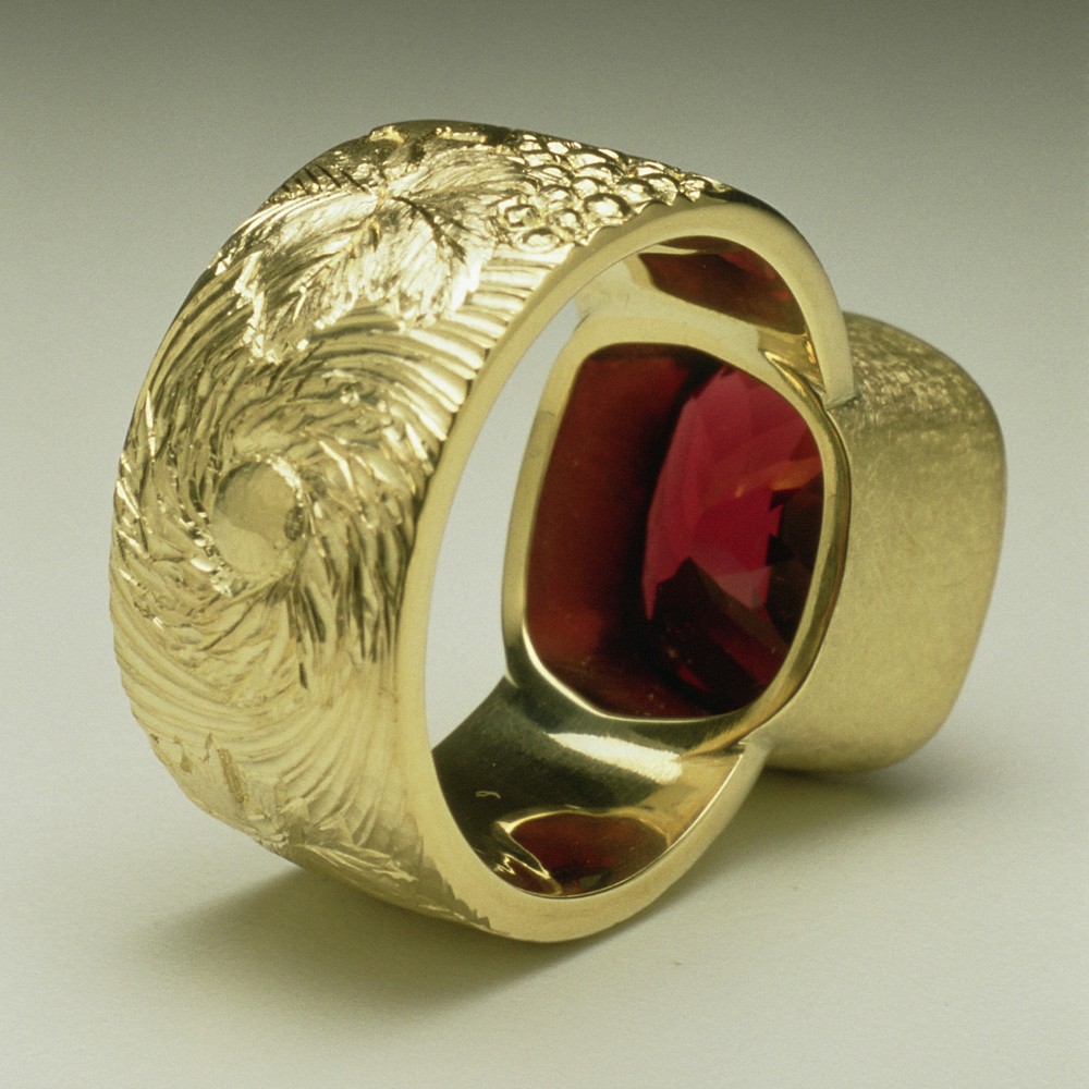 18ct yellow gold, hand engraved and carved with vine leaves and grapes, cushion cut garnet. (Back image)