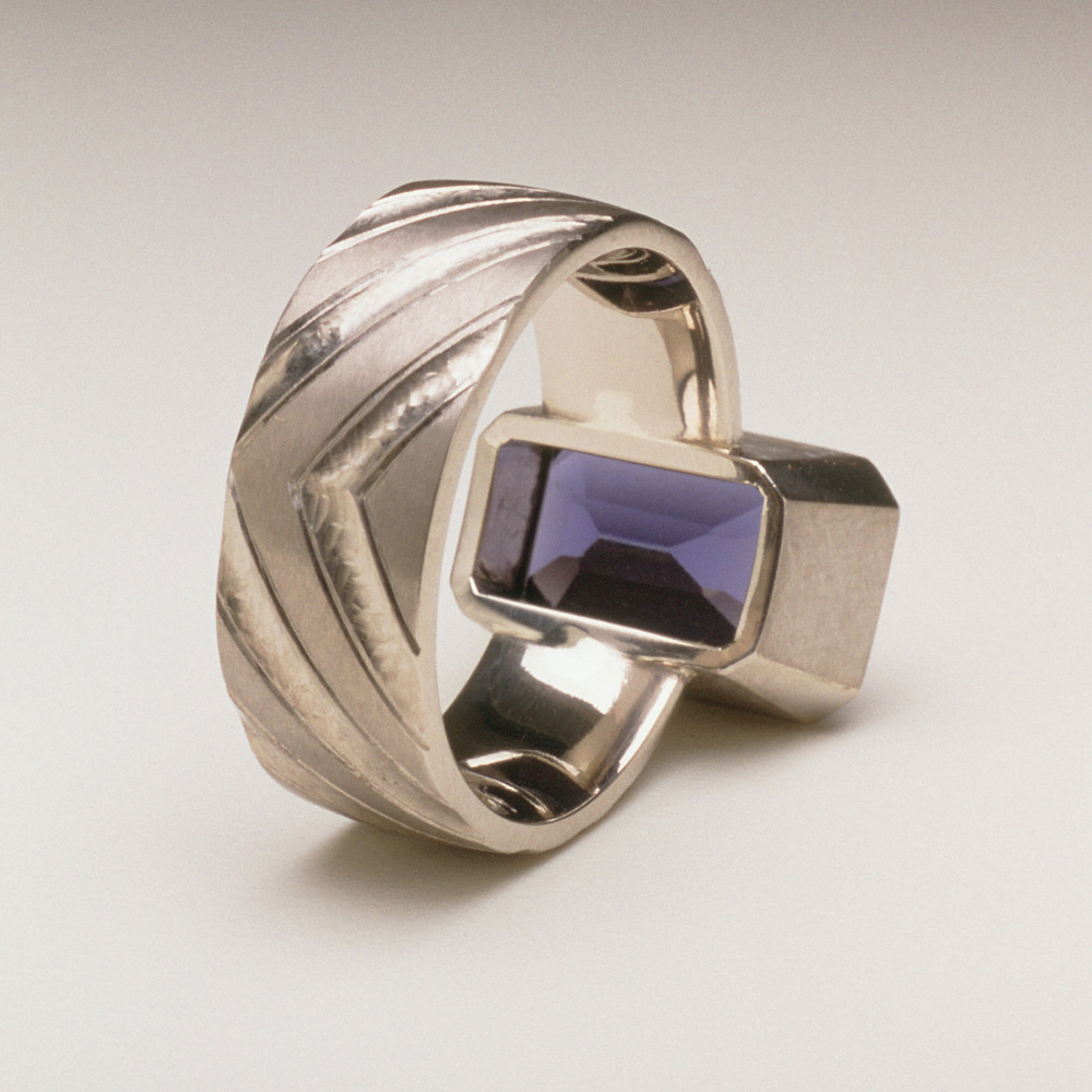 <a href="/jewellery/reverse-detail-8">Reverse Detail: Ring shank inspired by pillars of the nave of Durham Cathedral. 18ct white gold, hand carved and engraved, setting a baguette Iolite.</a>