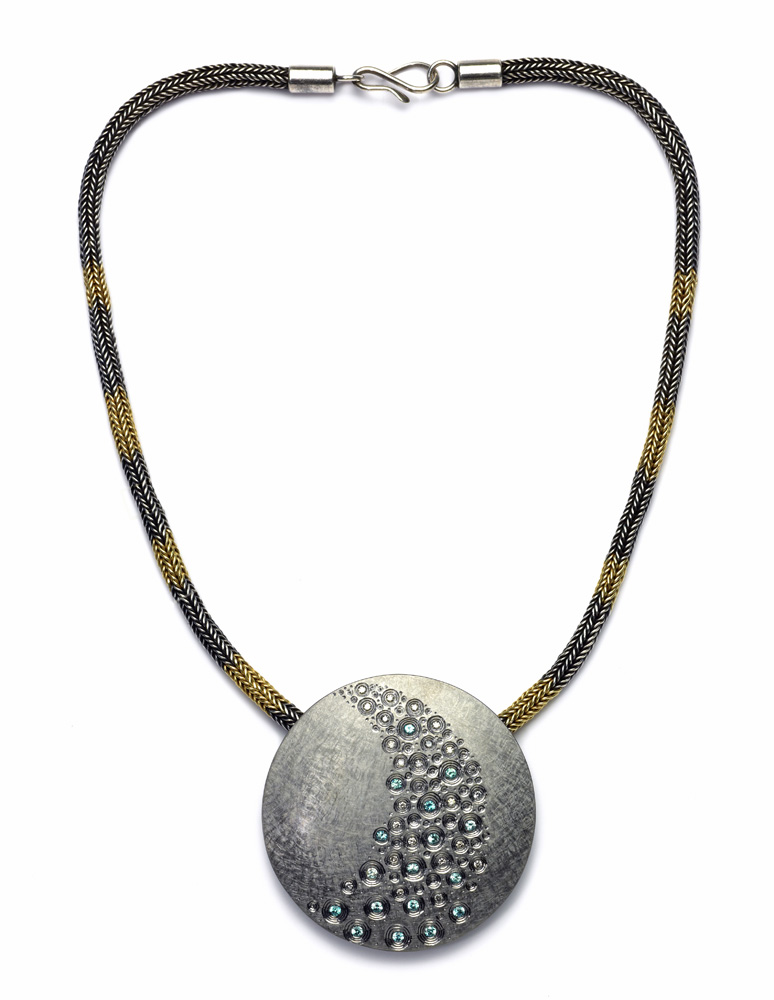 Silver, hand engraved, finished in grey rhodium, set with pale blue zircons and grey diamonds.  60mm diameter.  2009. Commission piece for use with existing hand-knitted, silver and green gold sacred knot chain acquired previously.  Photo: Simon B Armitt.