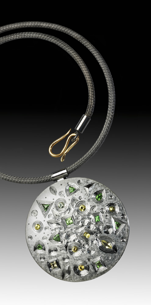 Silver, hand engraved, finished in grey rhodium plate. Set with yellow and grey sapphires, and green garnets. Approximately 60 mm diameter. 2009/10. Chain: silver, grey rhodium plated. Photo Simon B Armitt.