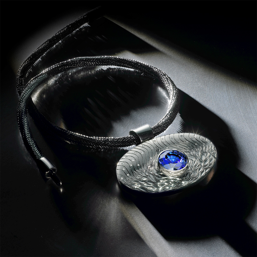 18ct white gold drop, hand engraved, set with tanzanite and white diamonds, pendant width 7.5cm. Oxidised, hand-knitted sacred knot silver chain with 18ct white gold clasp. Photo : Paul Hartley.