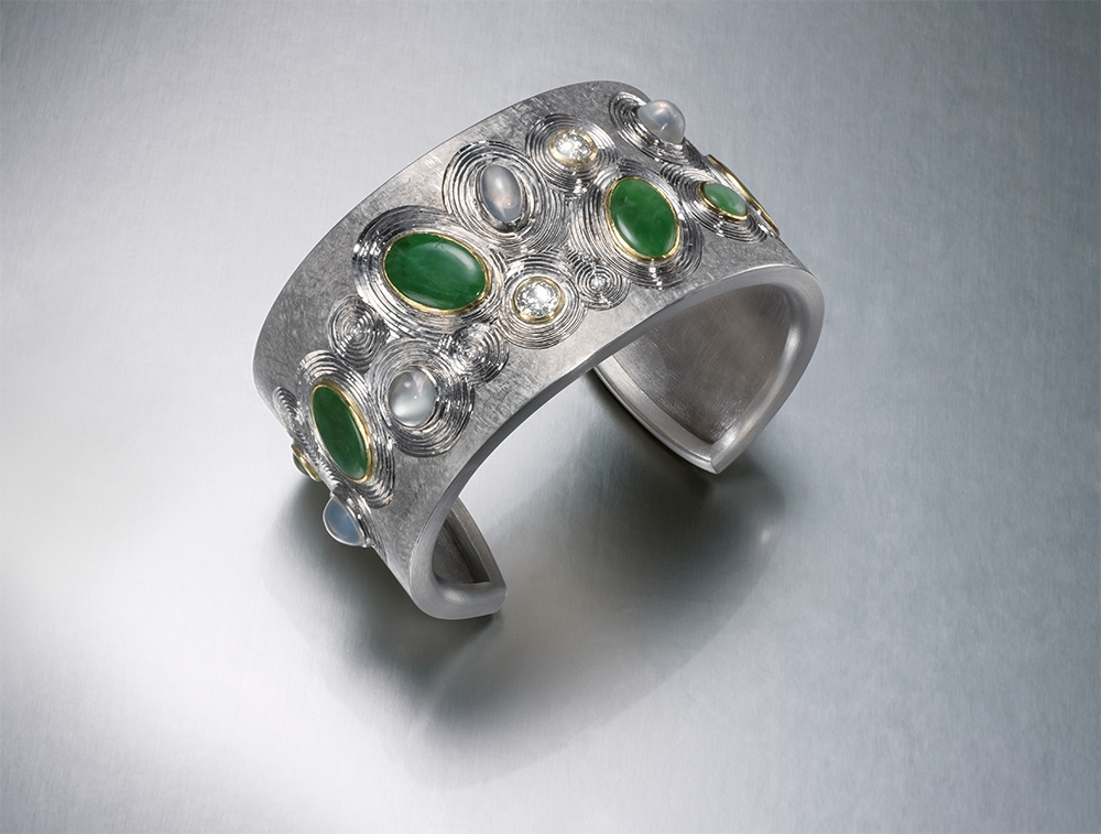 Silver, hand engraved, finished in grey rhodium, set with  family stones - oval jades, diamonds, moonstones. 7 cm across, 3.5 cm wide. Photo Simon B Armitt