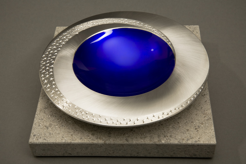 Angle view: STARLIGHT BOWL 150 mm diameter. Britannia Silver. Blue Enamel, Hand Engraved. Brushed and striated finish. Base polished Limestone. Bowl is designed to spin gently on its stone base. Photo : Simon Armitt